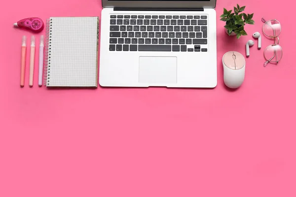 Laptop, computer mouse and stationery on pink background
