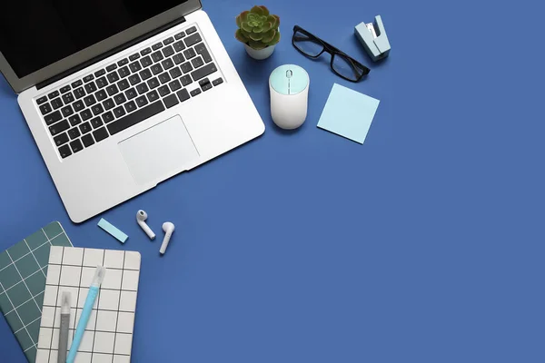 Laptop, computer mouse and stationery on blue background