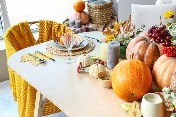 Autumn setting with pumpkins and flowers on dining table in room