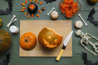 Yeşil ahşap masada Cadılar Bayramı süsleriyle oyulmuş balkabağı.