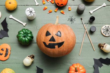 Yeşil ahşap masada Cadılar Bayramı süsleriyle boyanmış balkabağı.