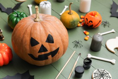 Yeşil ahşap masada Cadılar Bayramı süsleriyle boyanmış balkabağı.