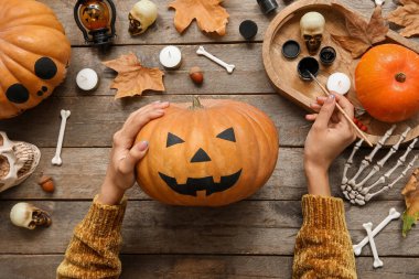 Ahşap masada boyalı Cadılar Bayramı kabağı taşıyan kadın.