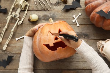 Ahşap masada Cadılar Bayramı balkabağı oyan kadın.