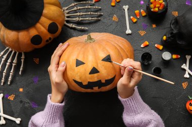 Cadılar Bayramı balkabağını siyah grunge masasında boyayan kadın.