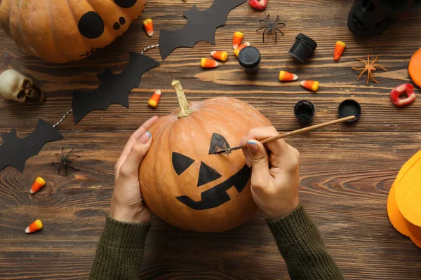 Ahşap masada Cadılar Bayramı balkabağı boyayan kadın.