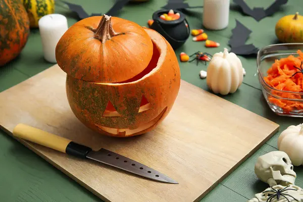 Yeşil ahşap masada Cadılar Bayramı süsleriyle oyulmuş balkabağı.