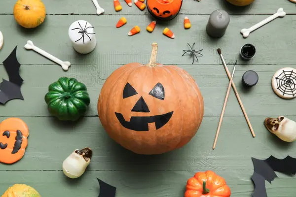 Yeşil ahşap masada Cadılar Bayramı süsleriyle boyanmış balkabağı.