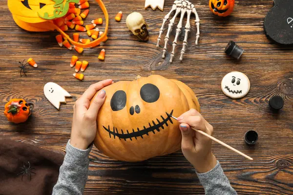 Ahşap masada Cadılar Bayramı balkabağı boyayan kadın.