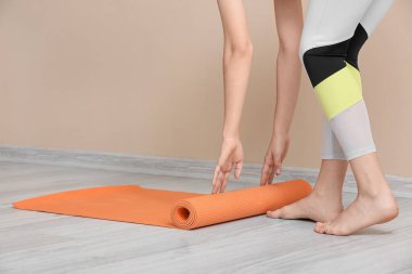 Spor salonundaki bej duvarın yanında yoga minderi olan sportif bir kadın.