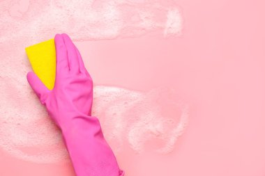 Pembe arka planda sünger ve köpük temizleyen kadın.