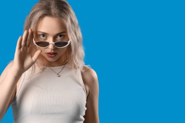 Mavi arka planda, şık güneş gözlüklü genç bayan, yakın plan.