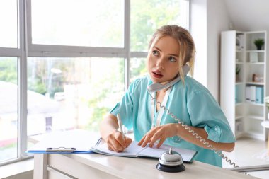 Klinikteki resepsiyonda telefonla konuşan kadın stajyer.