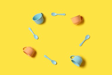 Sarı zemin üzerinde bebek için farklı fincan ve kaşıklardan yapılmış çerçeve