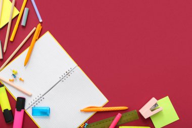 Kırmızı arkaplanda boş defter ve farklı kırtasiye malzemesi olan kompozisyon