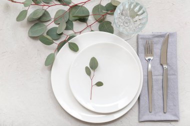 Gri masa üzerinde temiz tabak, çatal bıçak takımı ve okaliptüs dallarıyla güzel bir masa.