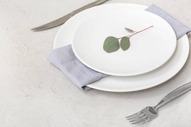 Gri masa üzerinde temiz tabak, çatal bıçak ve okaliptüs dallarıyla güzel bir masa.