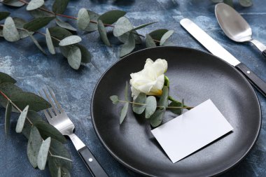 Boş davetiye kartı, östoma çiçeği ve mavi masadaki okaliptüs dallarıyla güzel bir masa.