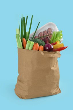 Mavi arka planda içi taze sebze ve sosis dolu kağıt torba.