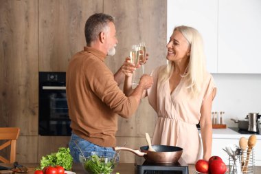 Olgun bir çift mutfakta şampanya içiyor.