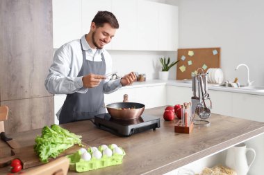 Genç adam mutfakta kızarmış sebzelere baharat katıyor.