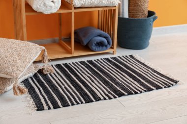 Turuncu duvarın yanında şık bir halı, yastıklar ve raf ünitesi