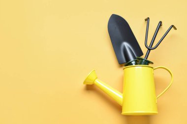 Sarı arka planda bahçe tırmığı ve kürekle teneke sulama.