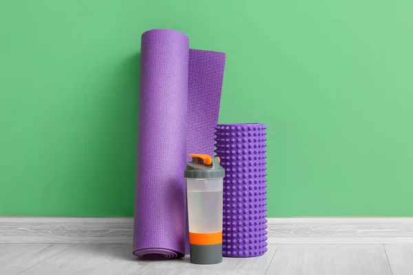 Yoga mat with foam roller and bottle near green wall in gym