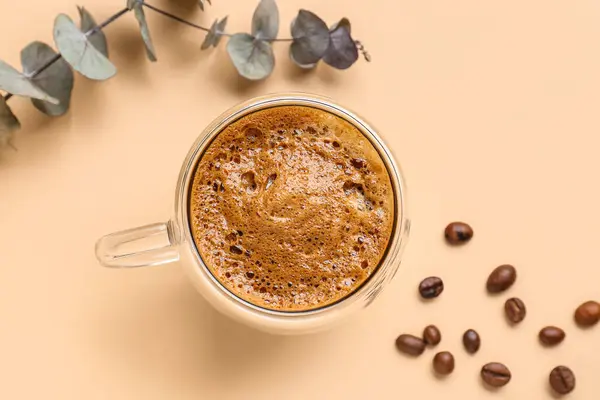 米色背景的一杯热咖啡和带有桉树的咖啡豆 — 图库照片