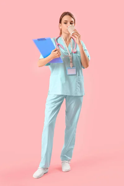ピンクの背景にコーヒーを飲むクリップボード付きの女性の医療インターン — ストック写真