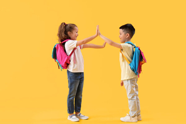 Cute little pupils giving each other high-five on yellow background