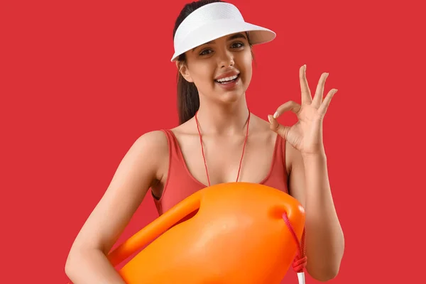 Female lifeguard with board showing OK on red background