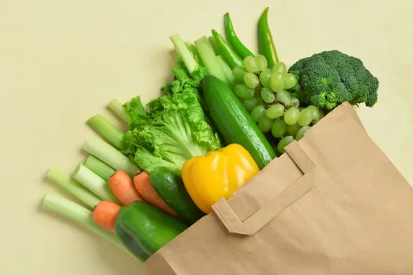 Paper bag with fresh vegetables and fruits on beige background