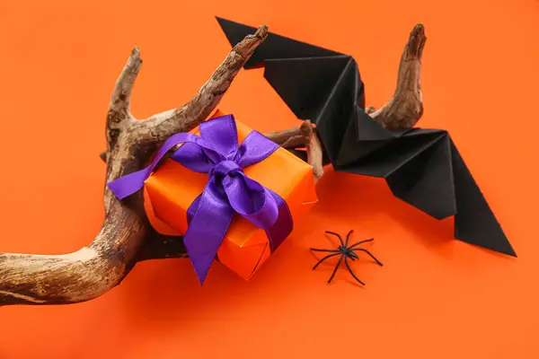 Composition with wood, bat and gift box for Halloween on orange background, closeup