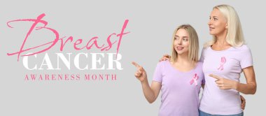 Pembe kurdeleli kadınlar gri arka plandaki bir şeyi işaret ediyorlar. Göğüs kanseri farkındalığı ayı