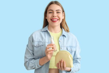 Makyaj temeli ve mavi arka planda makyaj çantası olan genç bir kadın.