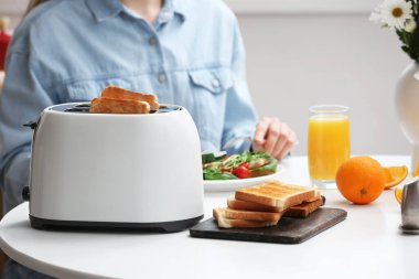 Kadın, modern ekmek kızartma makinesi, kıtır ekmek dilimleri ve portakal suyuyla kahvaltı yapıyor.