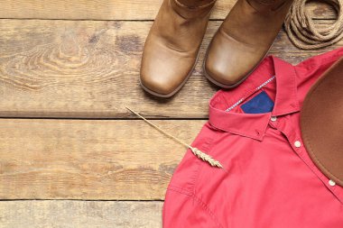 Kovboy çizmeleri, şapka ve kırmızı gömlek ahşap arka planda.