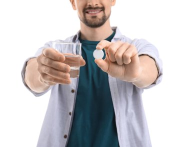 Beyaz arka planda çözünür tableti ve bir bardak suyu olan genç adam, yakın plan.