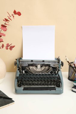 Kalem tutacağı, defter ve vazo içeren klasik daktilo bej duvarın yanındaki masada.