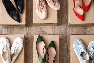 Farklı kadın topuklu ayakkabı ve tahta arka planda spor ayakkabıları olan karton kutular.