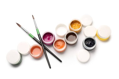 Kavanozlar dolusu renkli guaj boyaları ve beyaz arka planda fırçalar.