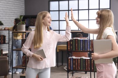 Bayan öğrenciler kütüphanede birbirlerine beşlik çakıyorlar.