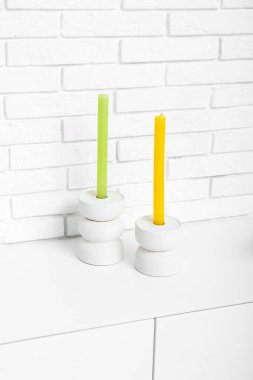 Beyaz çekmeceler, odada hafif tuğla duvarın yanında mumlar, yakın plan.