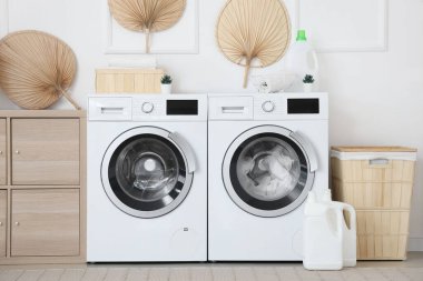 Çamaşır makinesi, ahşap dolap ve çamaşır sepetinin olduğu çamaşır odasının içi.