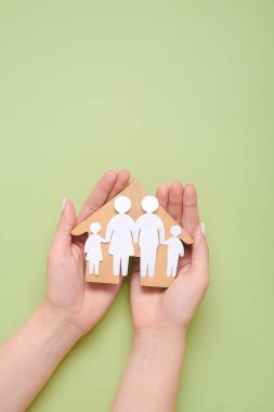 Yeşil arka planda aile ve ahşap ev figürleri tutan bir kadın.