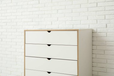 Odanın hafif tuğlalı duvarının yanındaki beyaz çekmeceler.