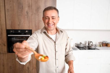 Olgun bir adam mutfakta kızarmış sebze tadıyor.