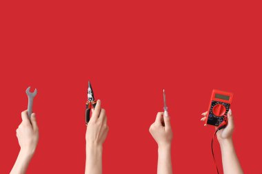 Kırmızı arkaplanda araçları olan elektrikçi elleri