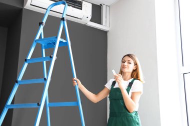 Kadın teknisyen odada klimayı açıyor.